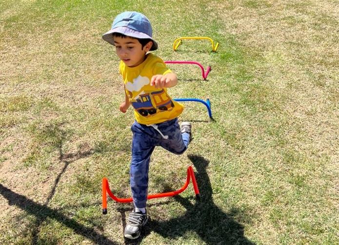  Little boy jumps over a hurdle wearing a wide-brimmed hat